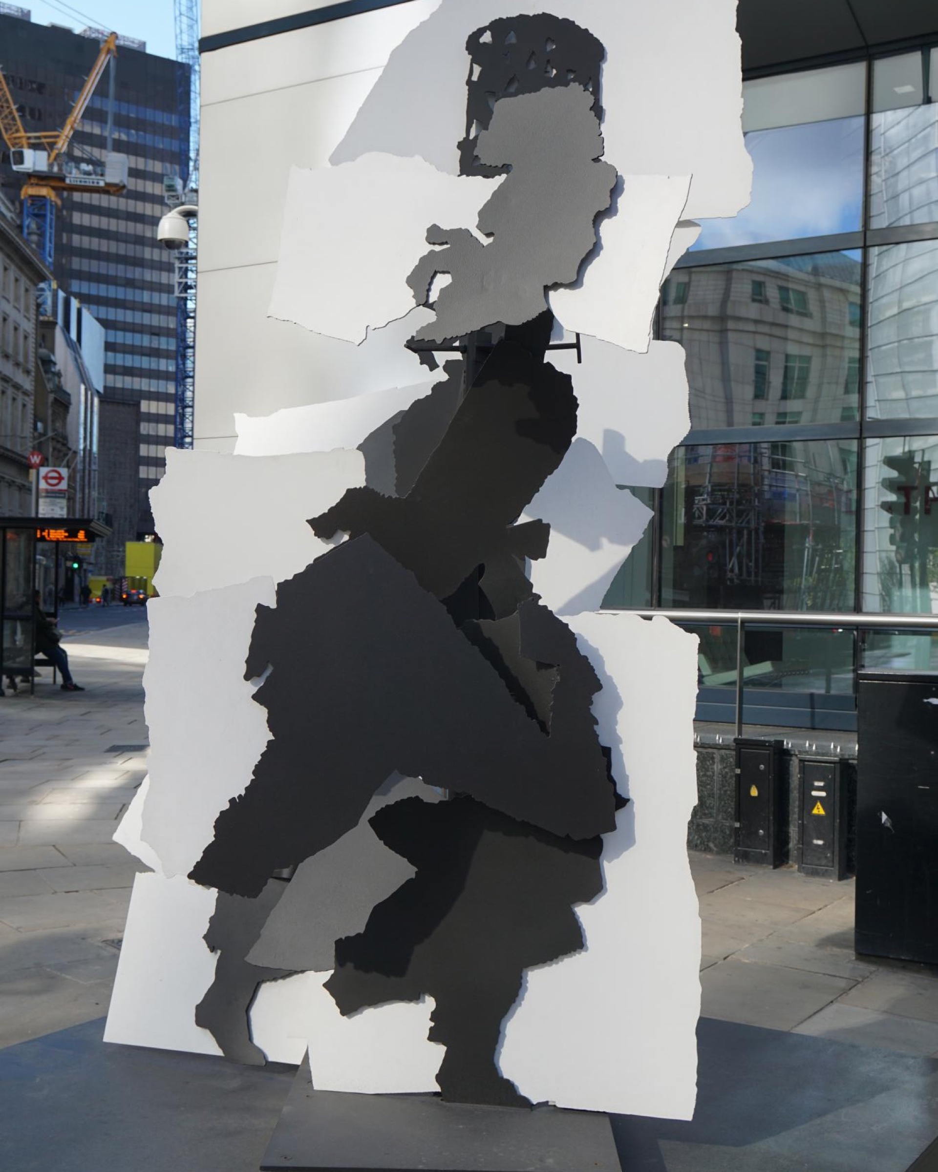 A tall cut-steel sculpture of a woman carrying a load on her head, painted in black, grey and white, on a City of London street