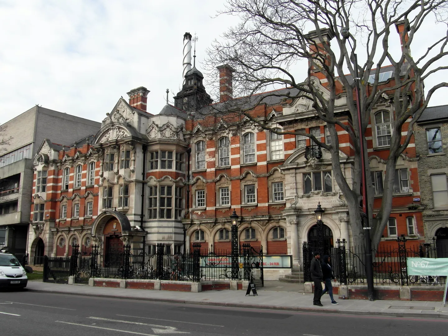Red-brick Victorian buildings on Peckham Road, with ornate gables and iron railings, under a pale sky