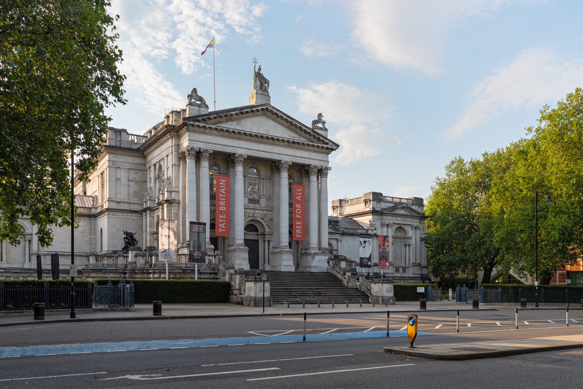Tate Britain on Millbank, with its portico, steps and exhibition banners, seen from across the road on a summer morning