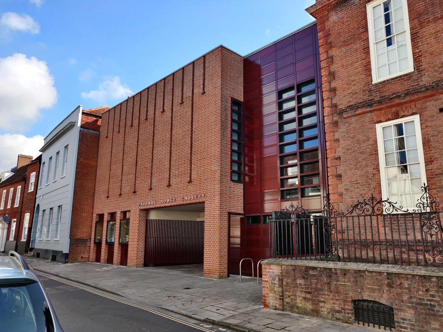 The red-brick front of Pallant House Gallery on a quiet street in Chichester, under a blue sky