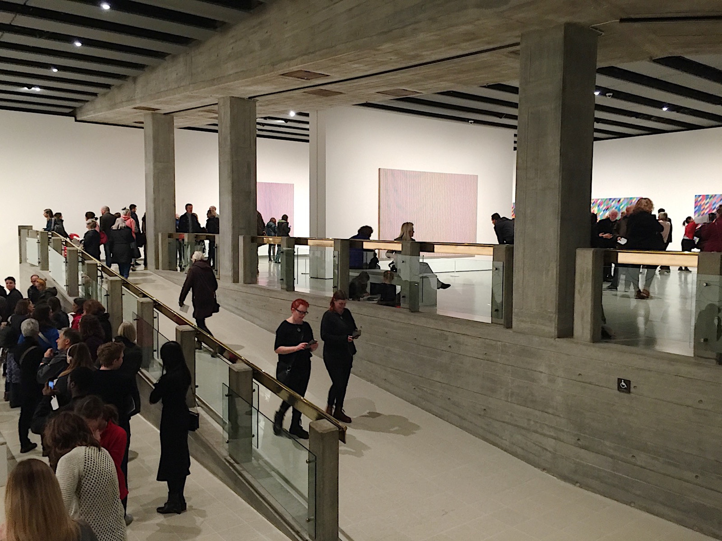 Visitors on the ramps and walkways of the Hayward Gallery's concrete galleries, with Riley's paintings on the walls