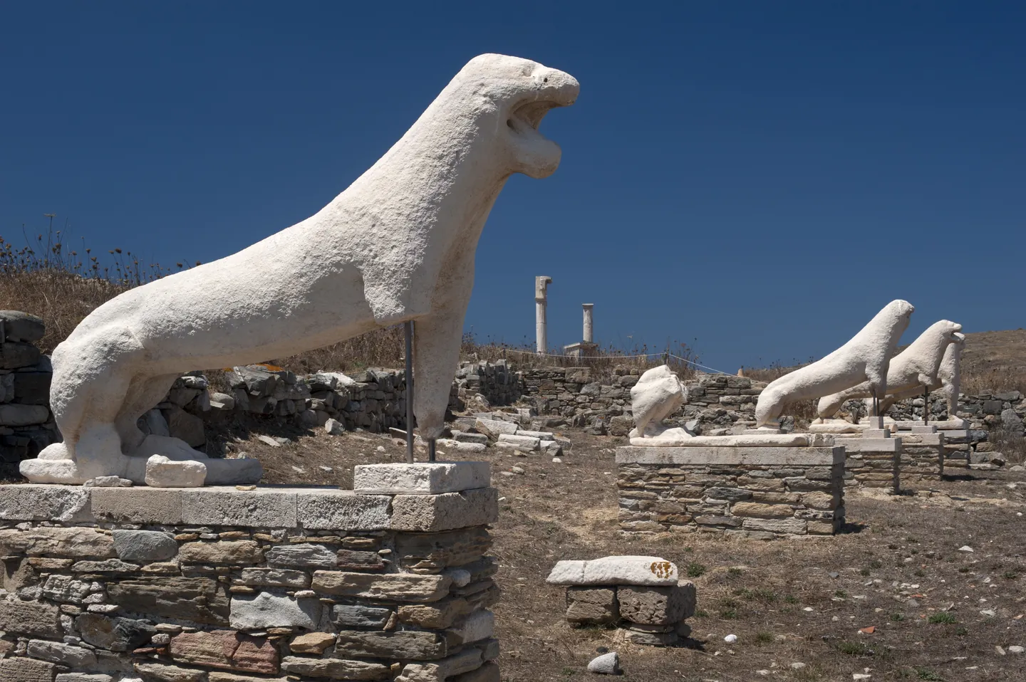 Marble lions of the seventh century BC standing in a row on stone bases on the island of Delos, under a deep blue sky