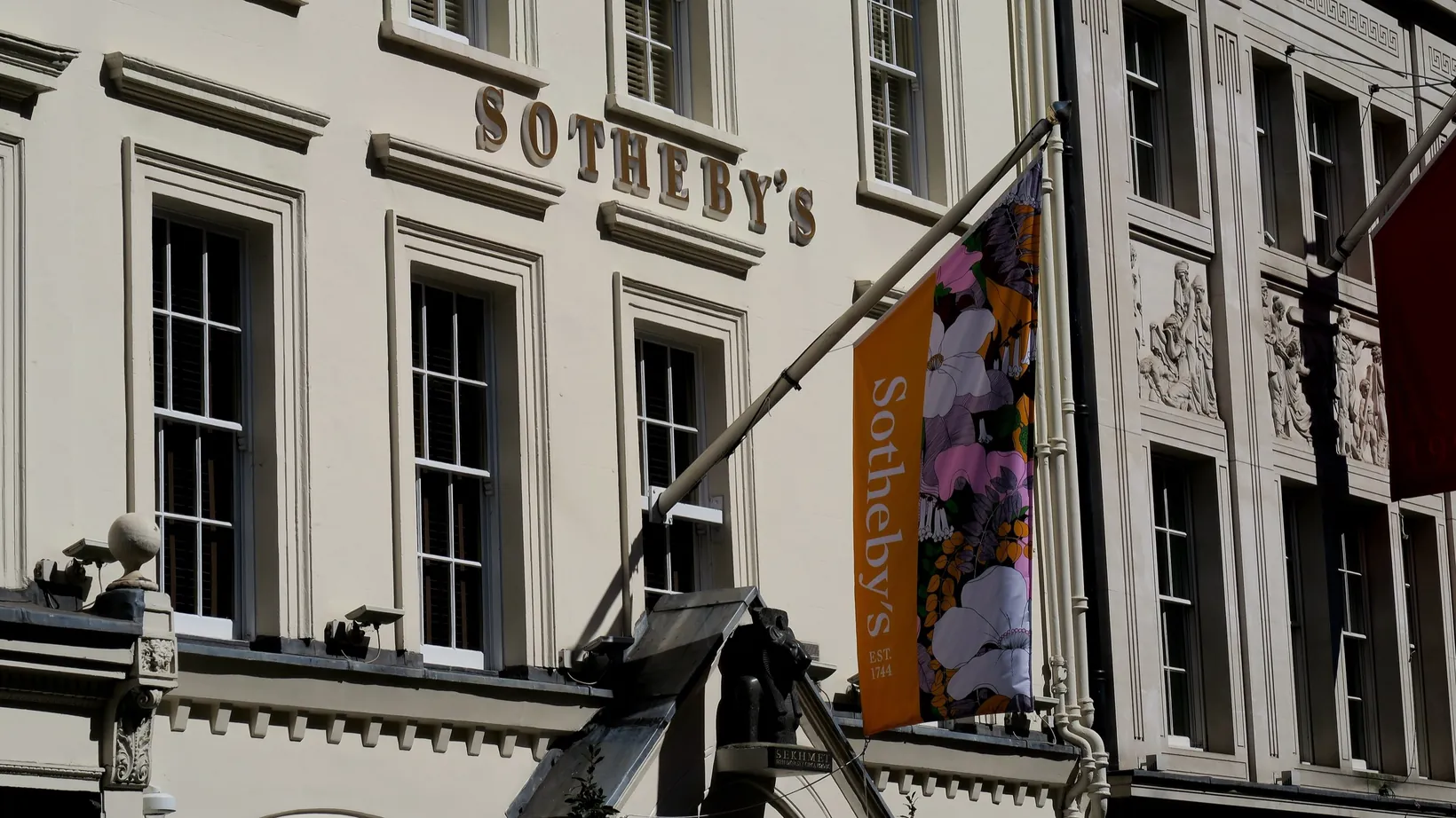 The cream stucco front of Sotheby's on New Bond Street, with its name in gold letters and an orange Sotheby's banner