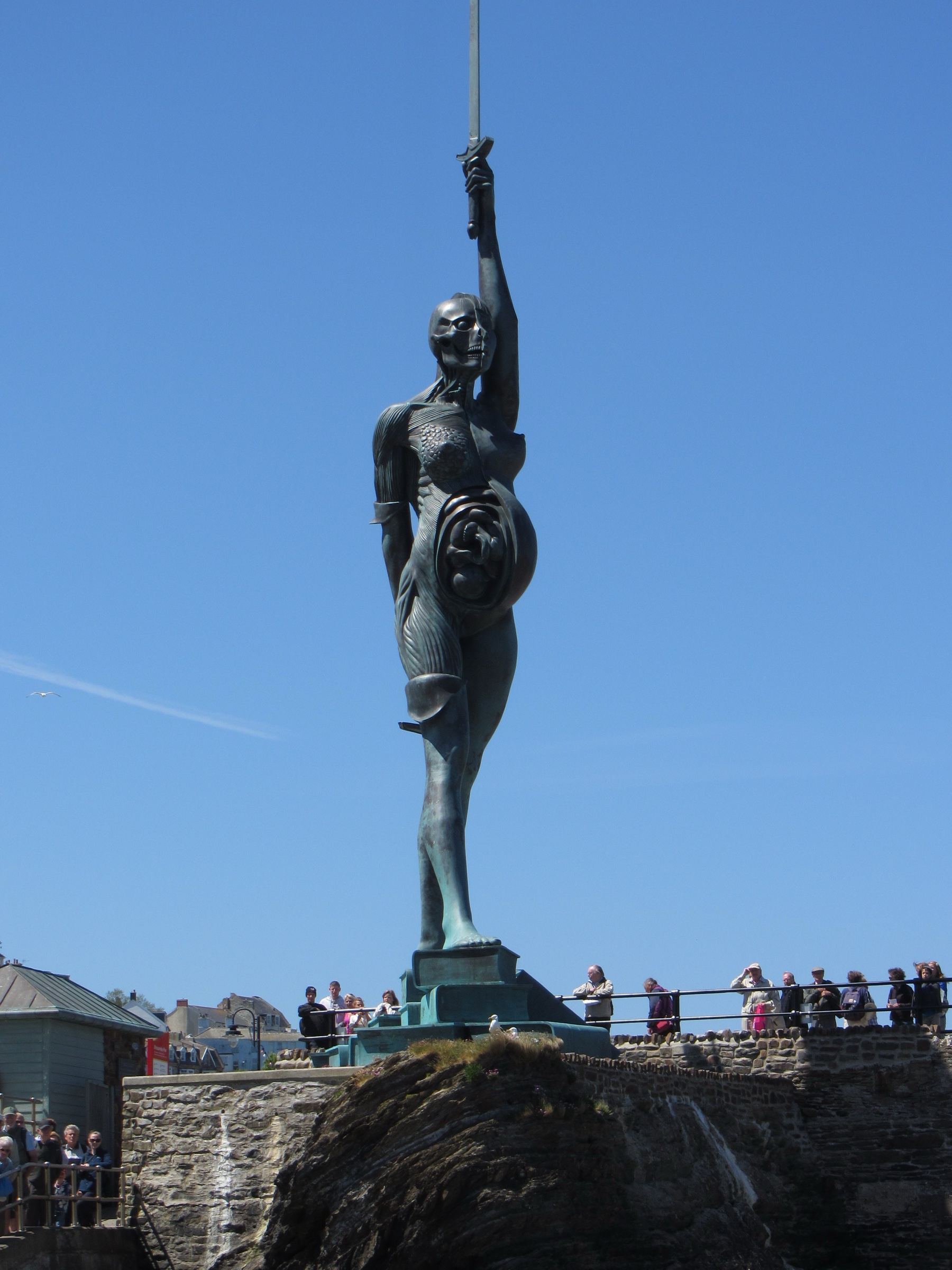 Damien Hirst's Verity, a giant bronze and steel figure of a pregnant woman holding a sword aloft, on the harbour wall at Ilfracombe with visitors at its base