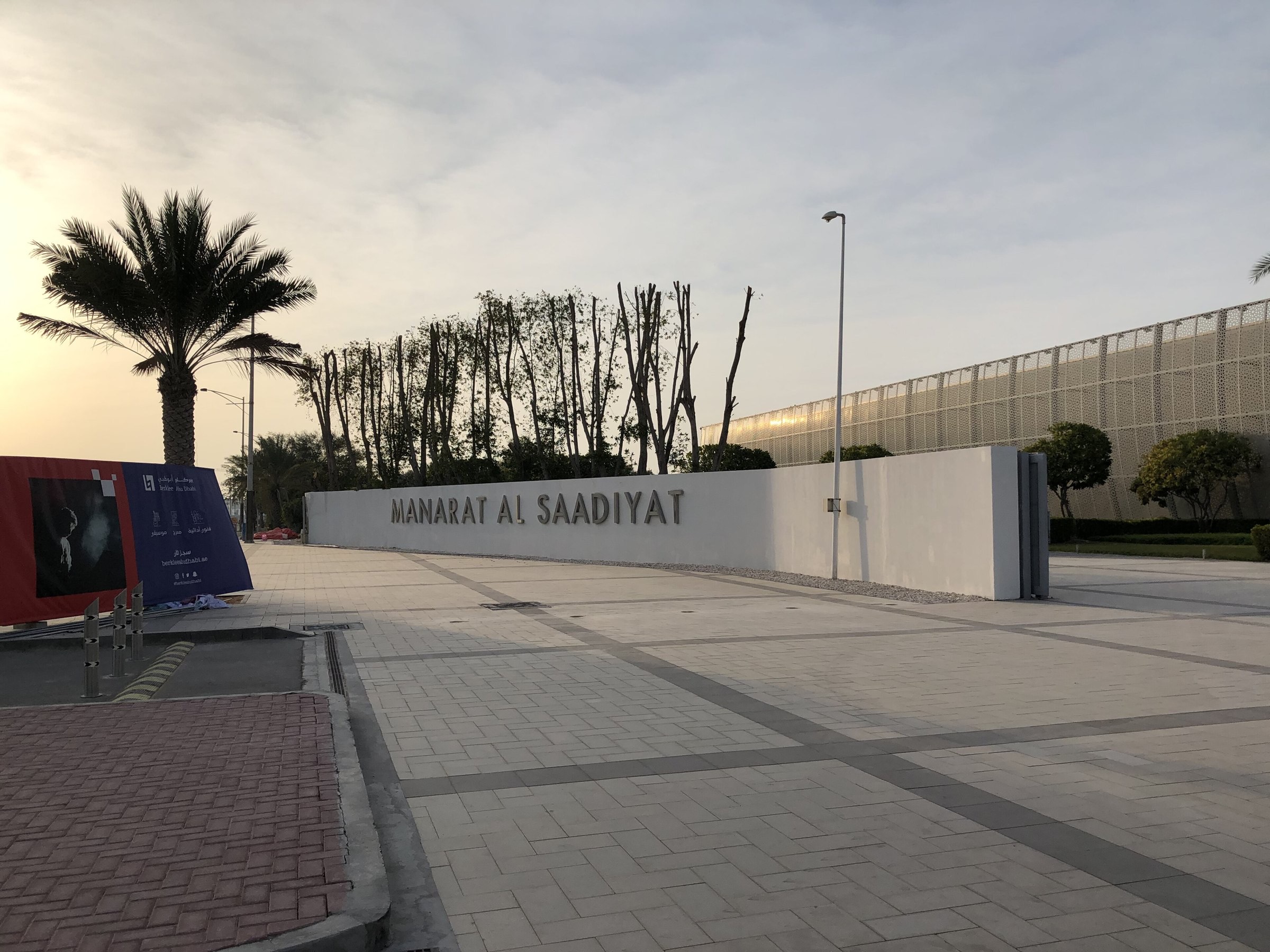 The entrance to Manarat Al Saadiyat in Abu Dhabi, with its name on a low white wall and palm trees behind