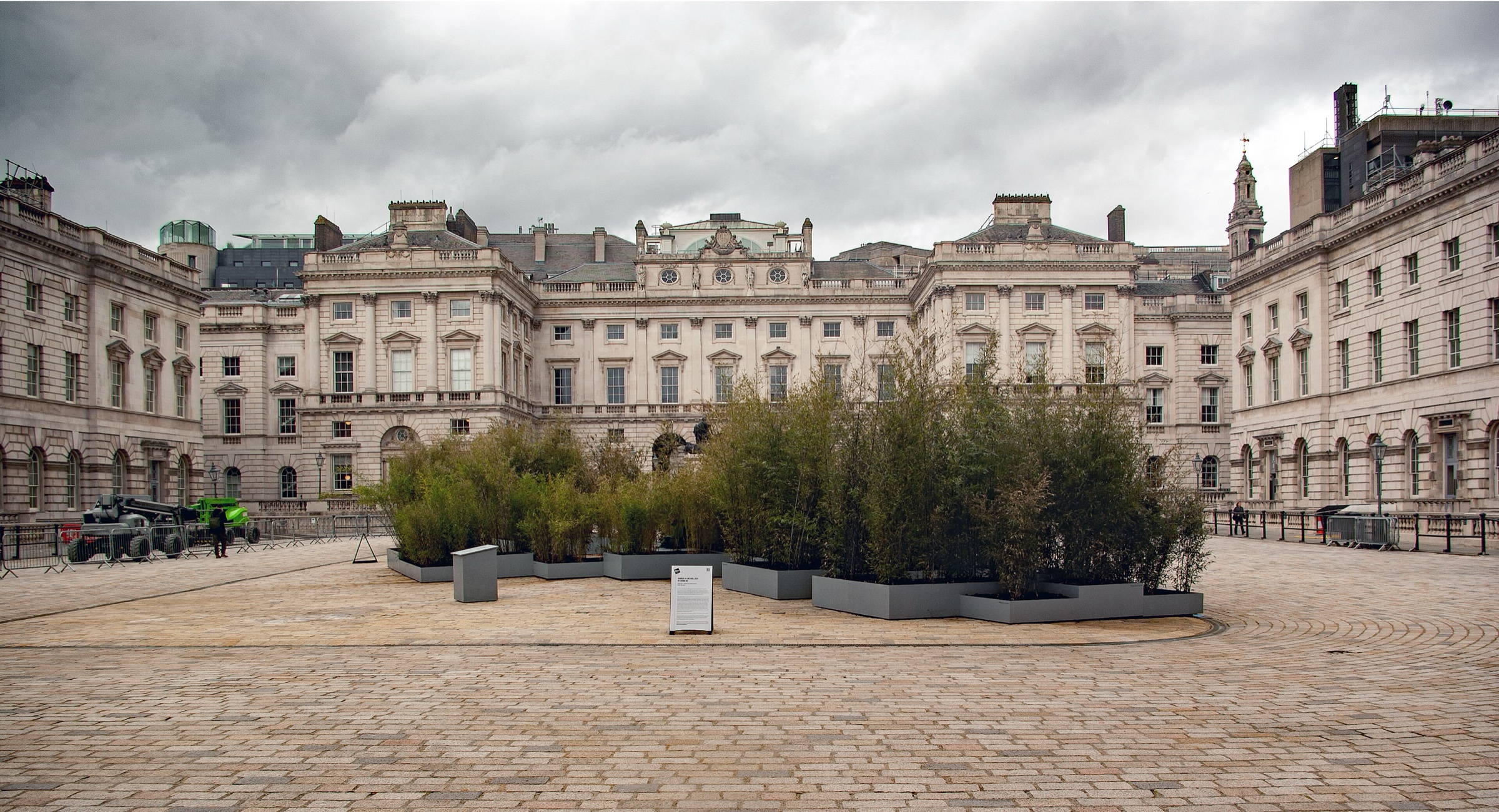 The wide stone courtyard of Somerset House under a cloudy sky, with a planted installation in the middle