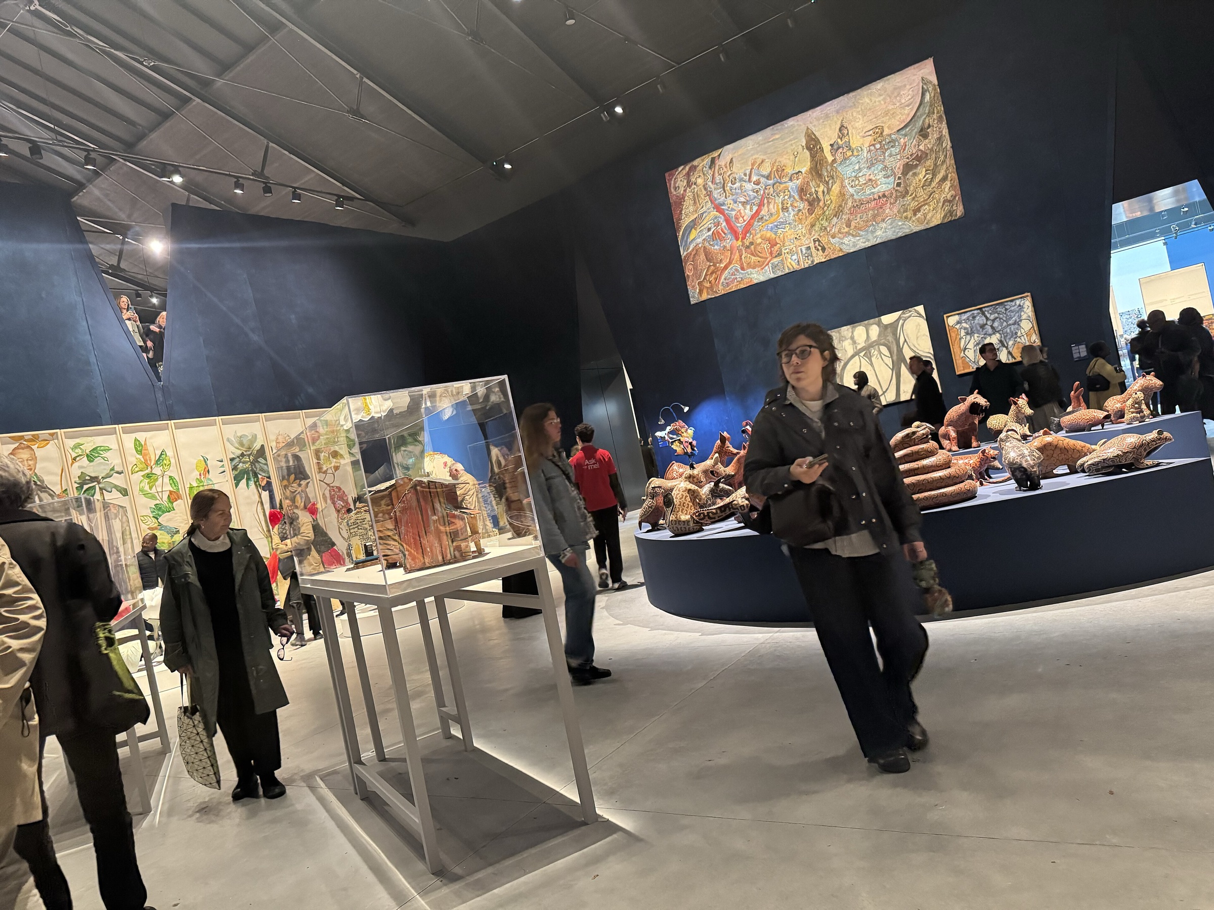Visitors among sculptures and paintings in a dark-walled gallery of the main exhibition in the Giardini