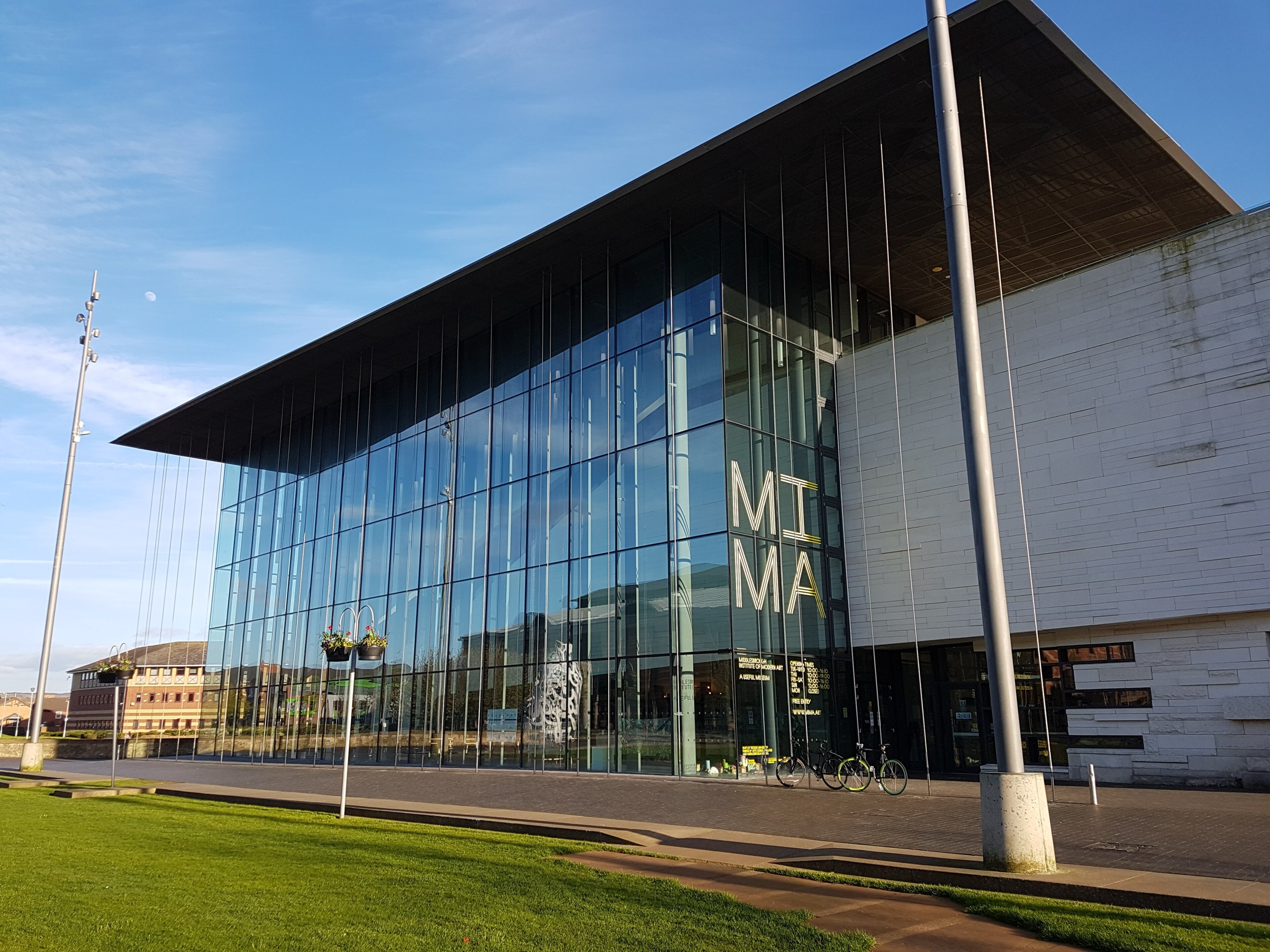 The glass and white stone front of MIMA on Centre Square in Middlesbrough, under a blue sky