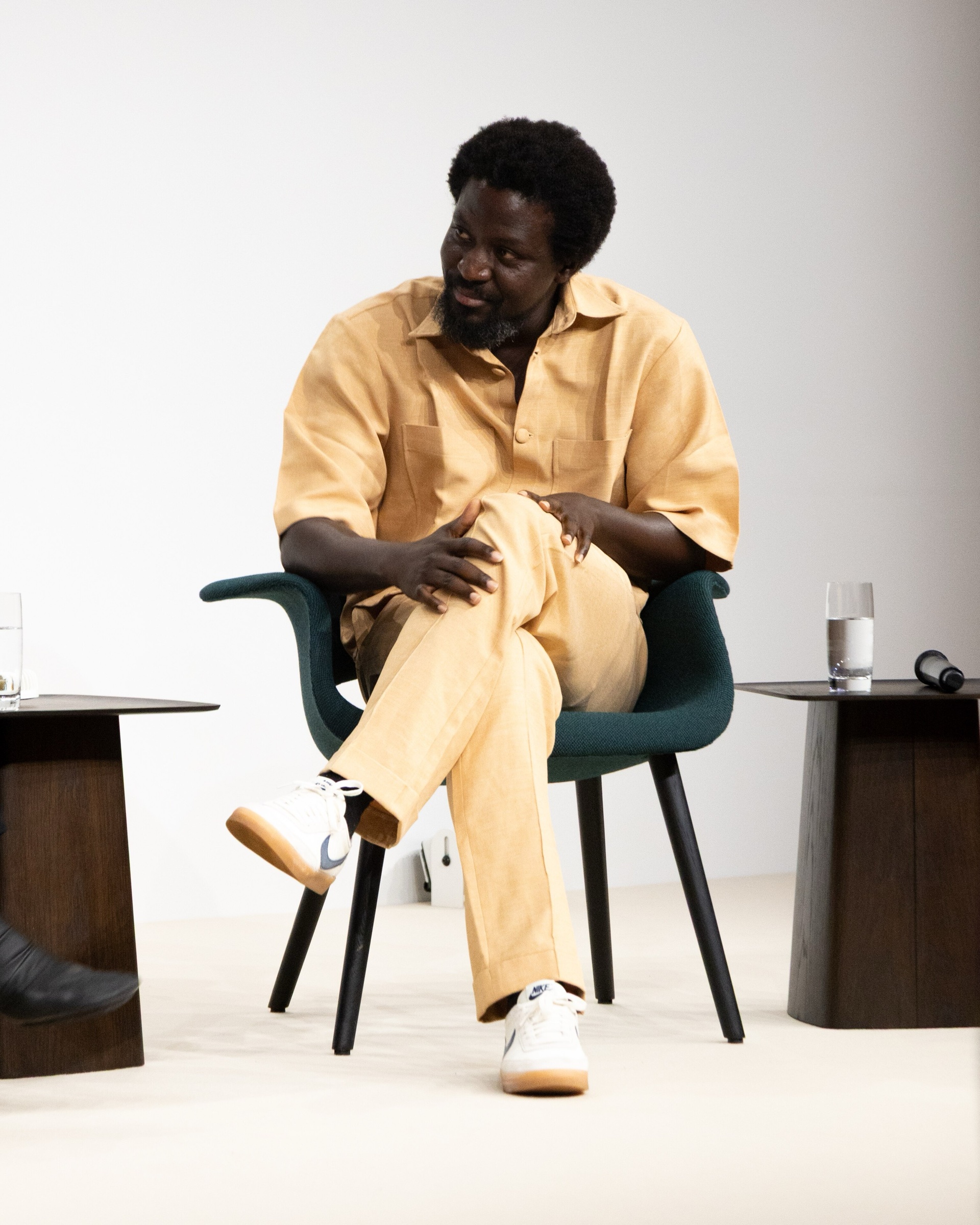 Ibrahim Mahama in a pale yellow shirt and trousers, seated on a stage in conversation