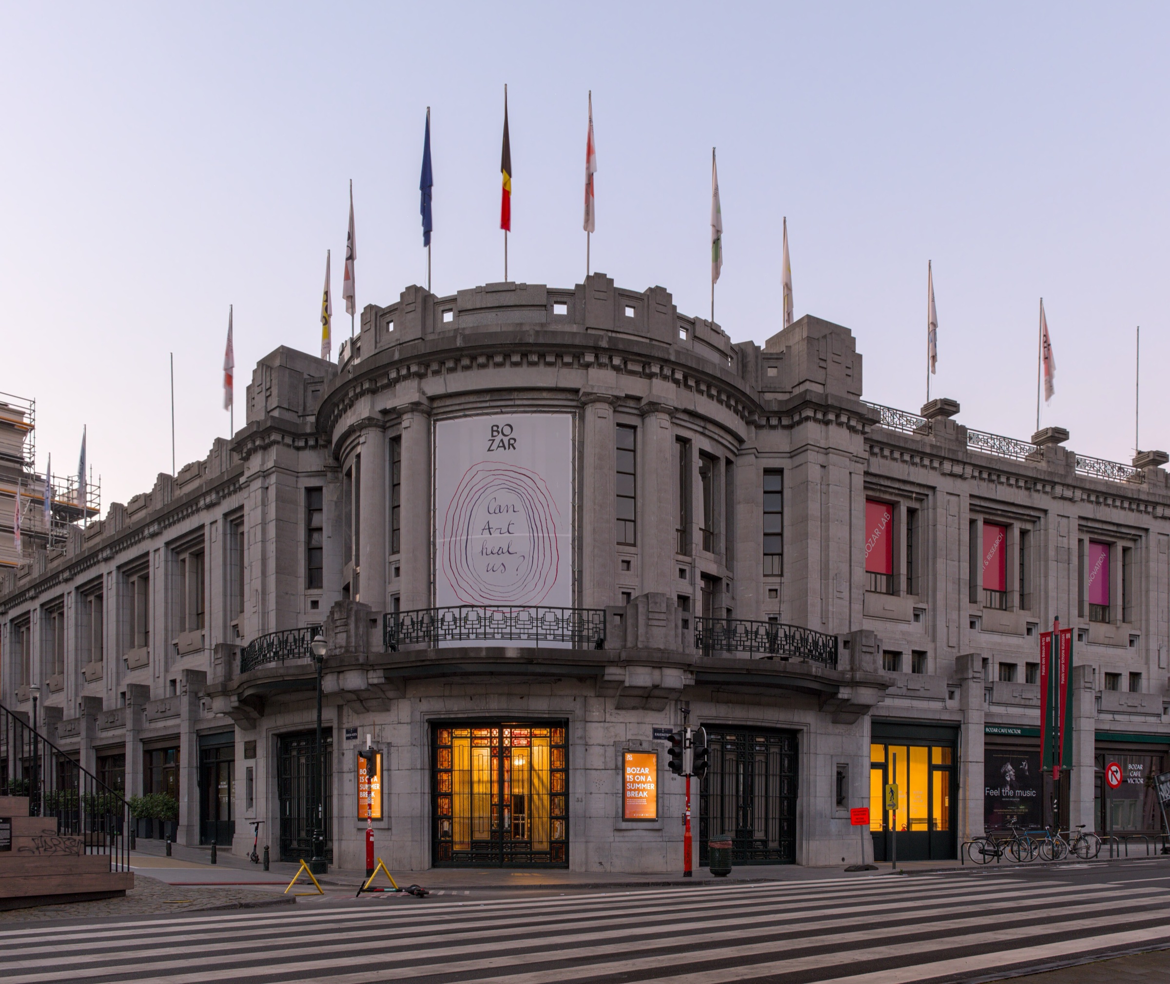 The domed corner entrance of Bozar in Brussels at dusk, with flags along the roofline