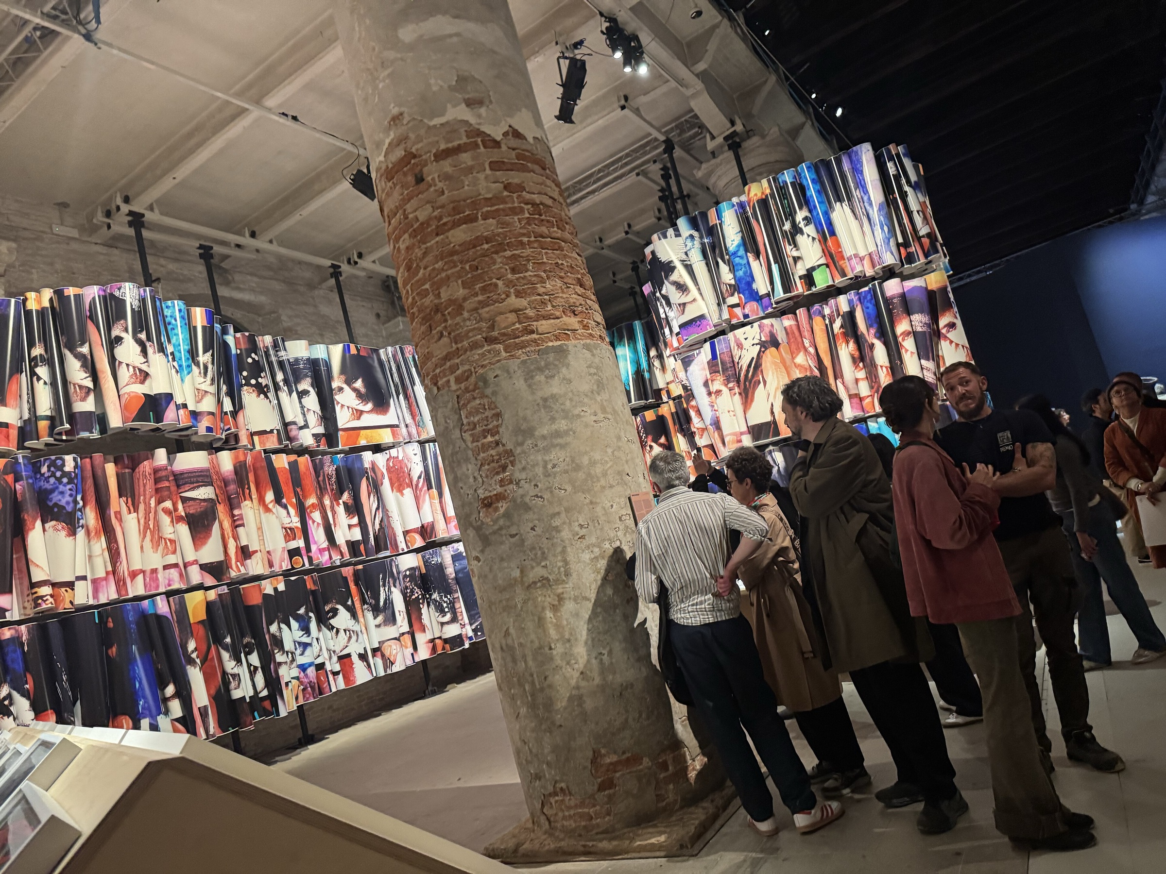 Visitors among brick columns in the Arsenale, with walls of hanging images behind them